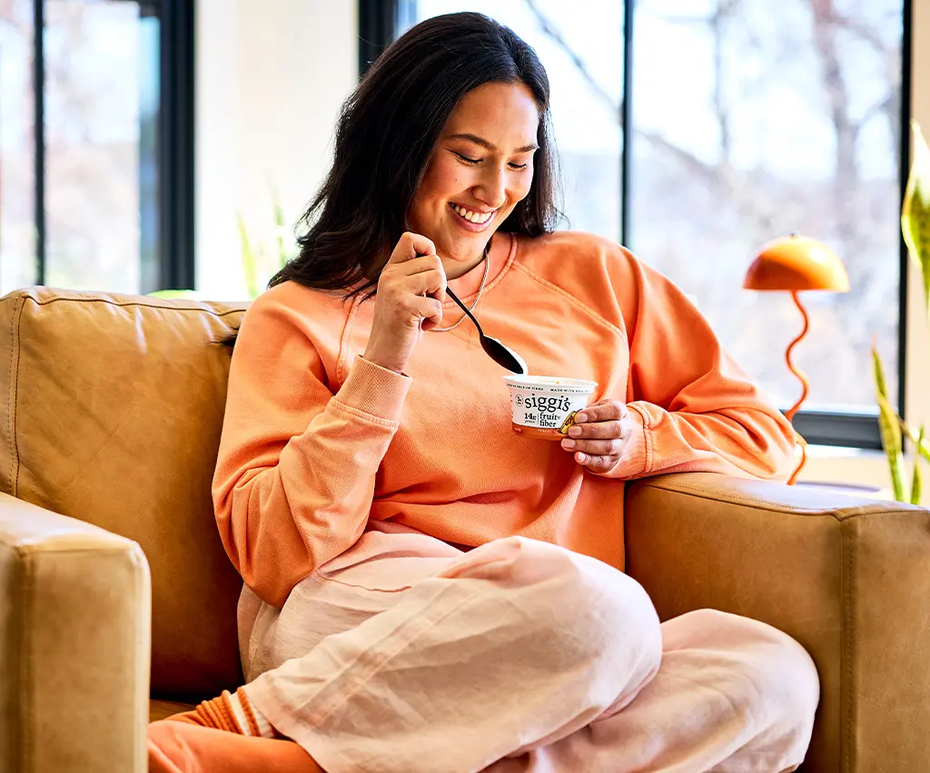 woman eating a siggi's fruit & fiber in a chair